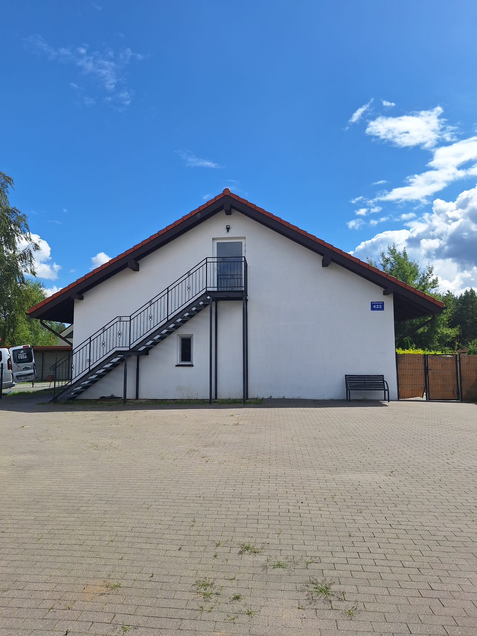 Obecny wygląd budynku: biała elewacja, zewnętrzne schody i pusty plac przed domem